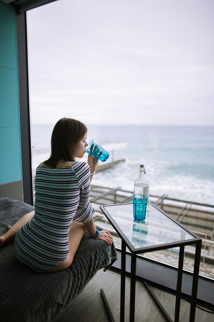 Rückansicht einer Frau beim Wassertrinken in einem Hotel mit Blick auf das Meer
