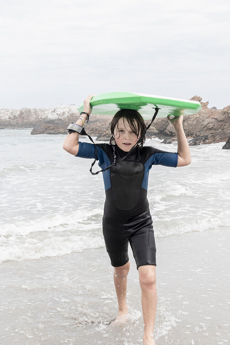 Boy (10-11) carrying bodyboard on Voelklip beach