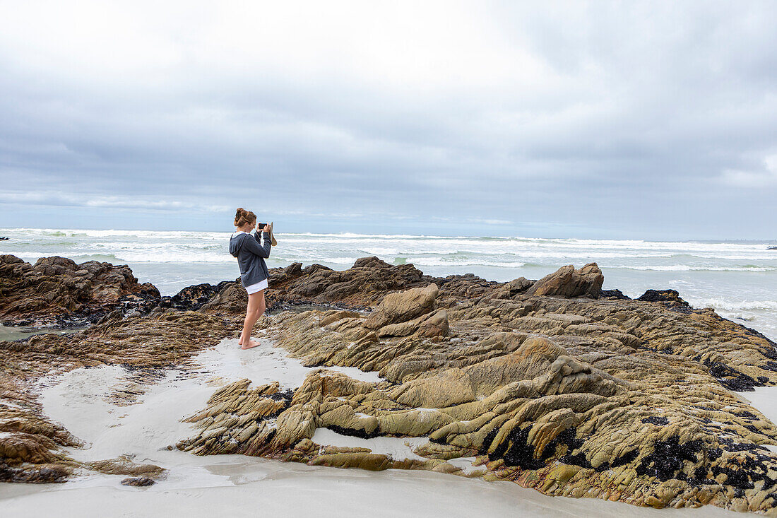 South Africa, Hermanus, Teenage girl (16-17) taking photos on Voelklip beach