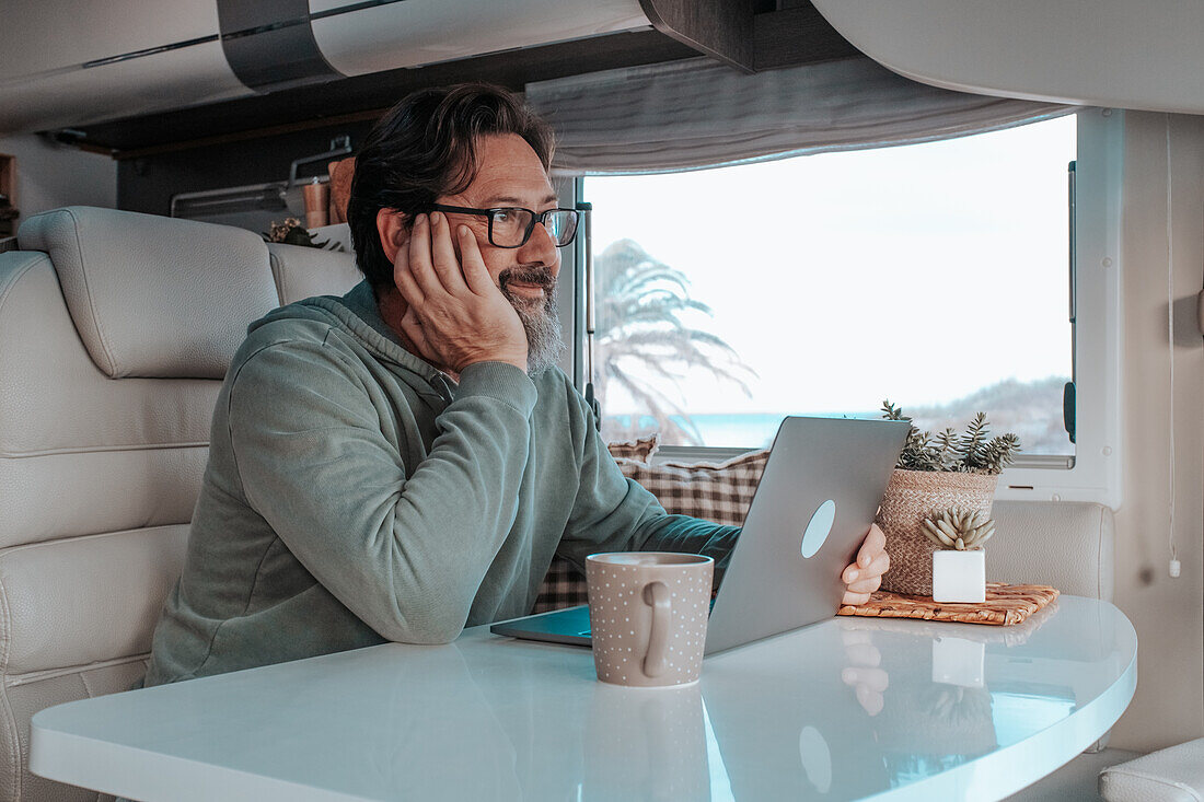 Mann sitzt im Wohnmobil und arbeitet am Laptop