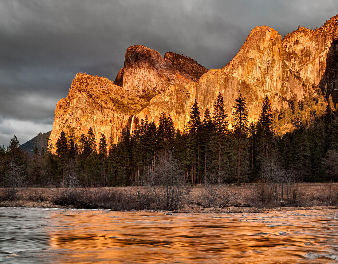 USA, Kalifornien, Yosemite National Park, Die untergehende Sonne beleuchtet den Bridalveil Fall und die Cathedral Rocks, die sich im Merced River spiegeln