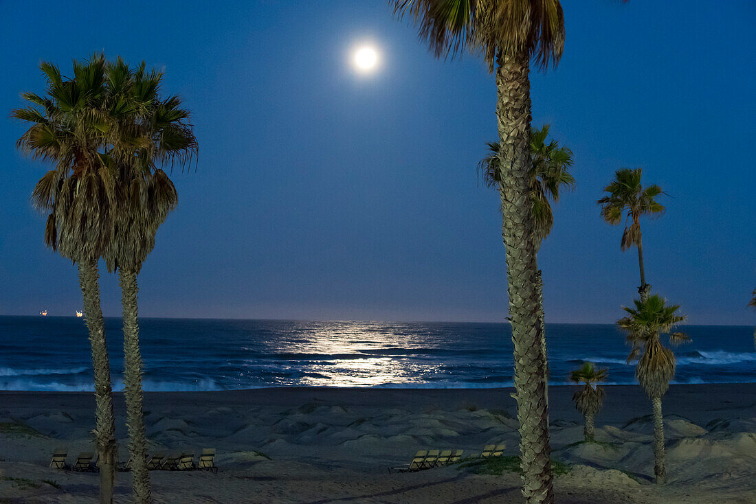 USA, Kalifornien, Oxnard. Mondlicht spiegelt sich bei Vollmond auf dem Pazifischen Ozean. Offshore-Ölplattformen leuchten am Horizont