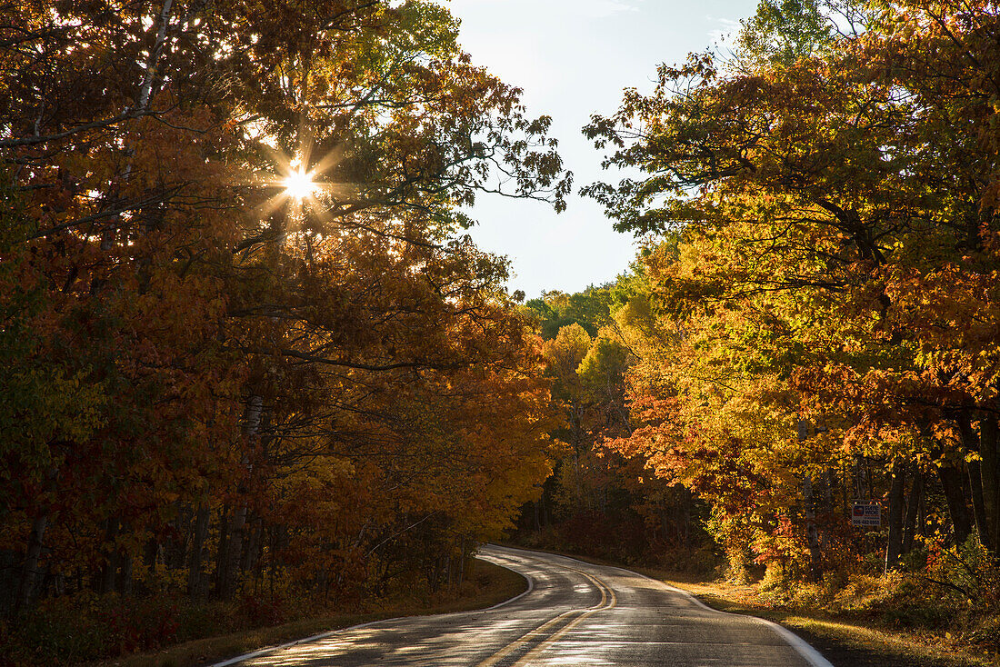 USA, Michigan. Das Sonnenlicht fällt durch das Herbstlaub entlang einer Landstraße auf der Keweenaw-Halbinsel.