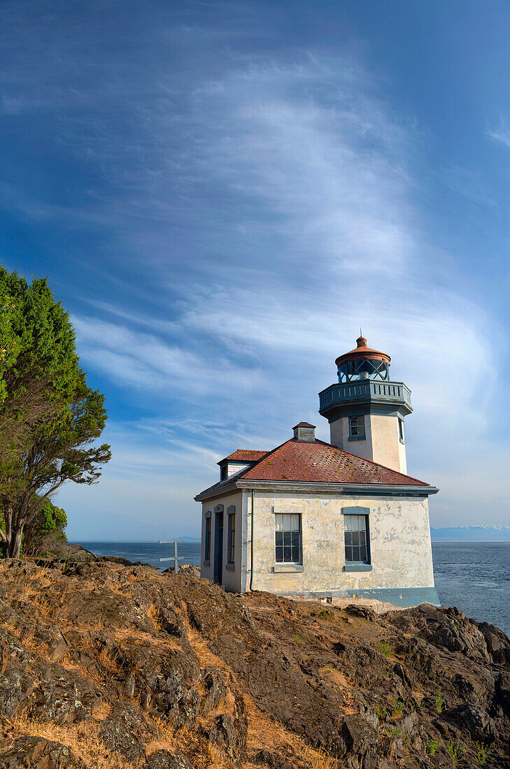 USA, Washington State, San Juan Island, Lime Kiln Point State Park, Lime Kiln Point Lighthouse and rocky shoreline beneath a cirrus filled sky.