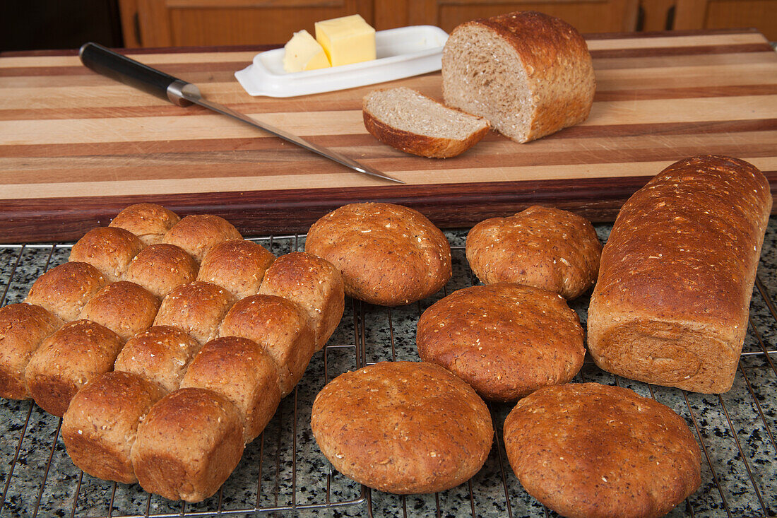 Multigrain rolls, buns and loaf with a slice cut off, with butter and a bread knife.