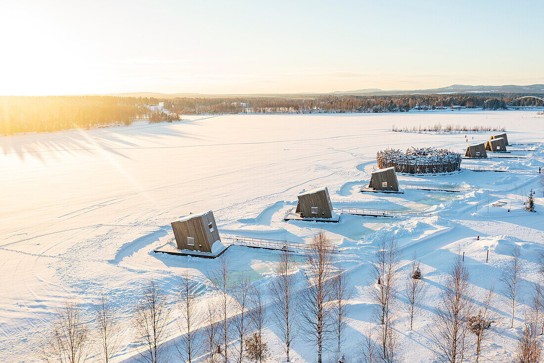 Die Holzhütten des luxuriösen Arctic Bath Spa Hotels schwimmen auf dem zugefrorenen, mit Schnee bedeckten Fluss Lule, Harads, Lappland, Schweden, Skandinavien, Europa