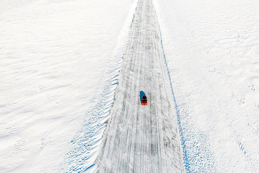 Kalte Wintersonne über einem einsamen Auto, das auf einer Eisstraße auf dem gefrorenen Meer fährt, Luftaufnahme, Lulea, Kreis Norrbotten, Lappland, Schweden, Skandinavien, Europa
