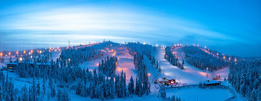Winterliche Abenddämmerung über den verschneiten Skipisten des Skigebiets Ruka, Luftaufnahme, Kuusamo, Nordösterbotten, Lappland, Finnland, Europa