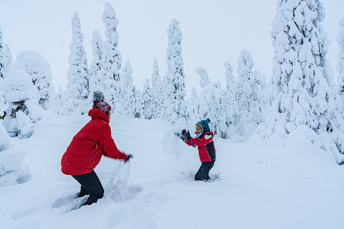 Fröhliche Mutter und Sohn spielen mit dem Schnee in der Winterlandschaft von Finnisch-Lappland, Finnland, Europa