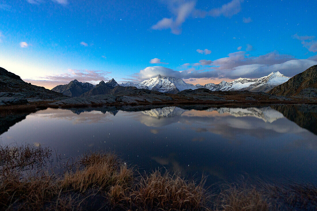 Verschneiter Gipfel des Monte Disgrazia spiegelt sich nachts im Wasser, Alpe Fora, Valmalenco, Valtellina, Provinz Sondrio, Lombardei, Italien, Europa