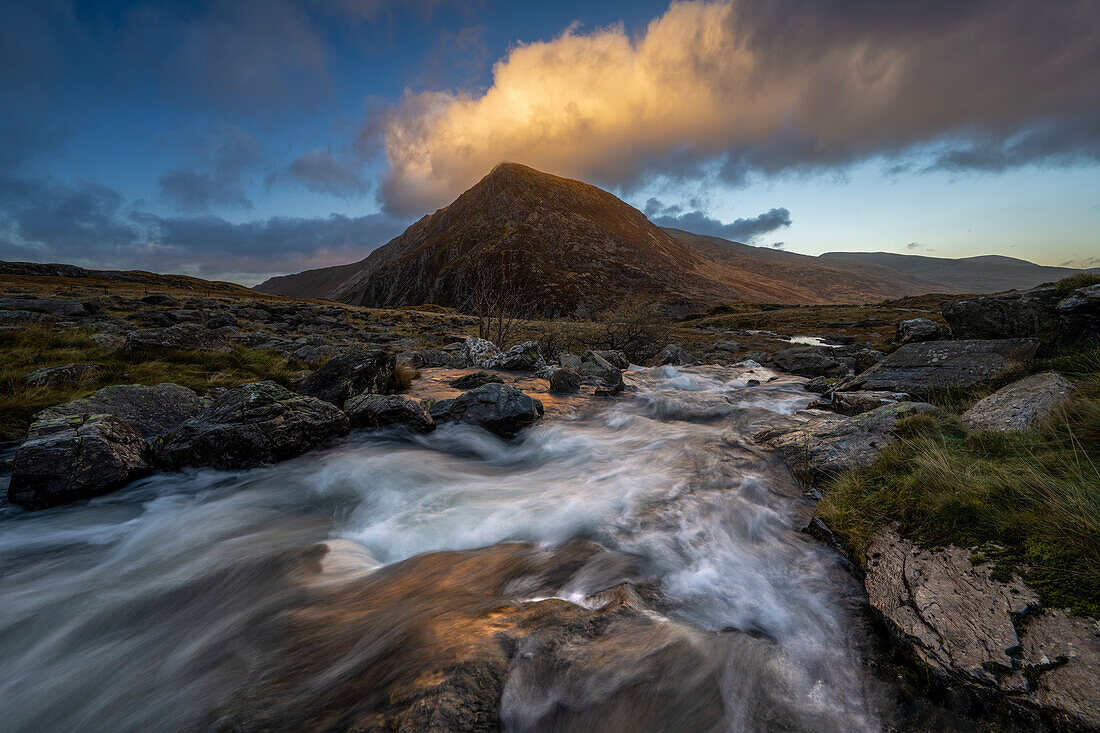 Wasser, das über einen Wasserfall in Richtung Llyn Dinas mit einer Bergkette im Hintergrund stürzt, Snowdonia, Wales, Vereinigtes Königreich, Europa