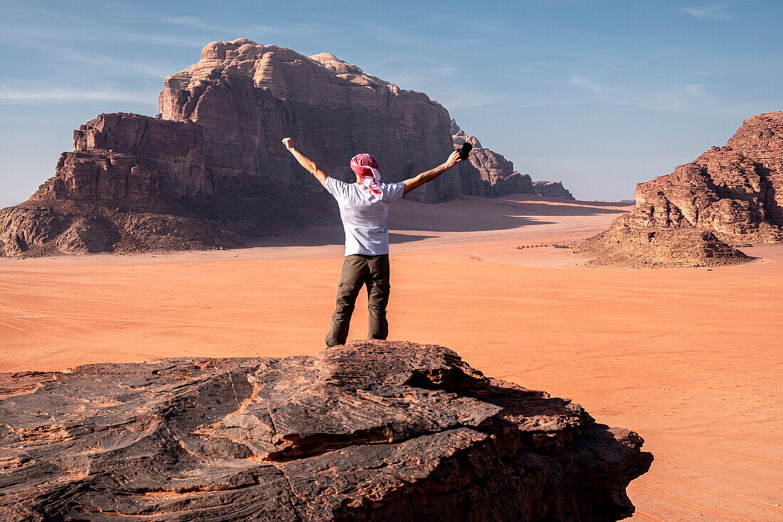 A man with a turban and his hands raised standing on a rock in the Wadi Rum desert, UNESCO World Heritage Site, Jordan, Middle East