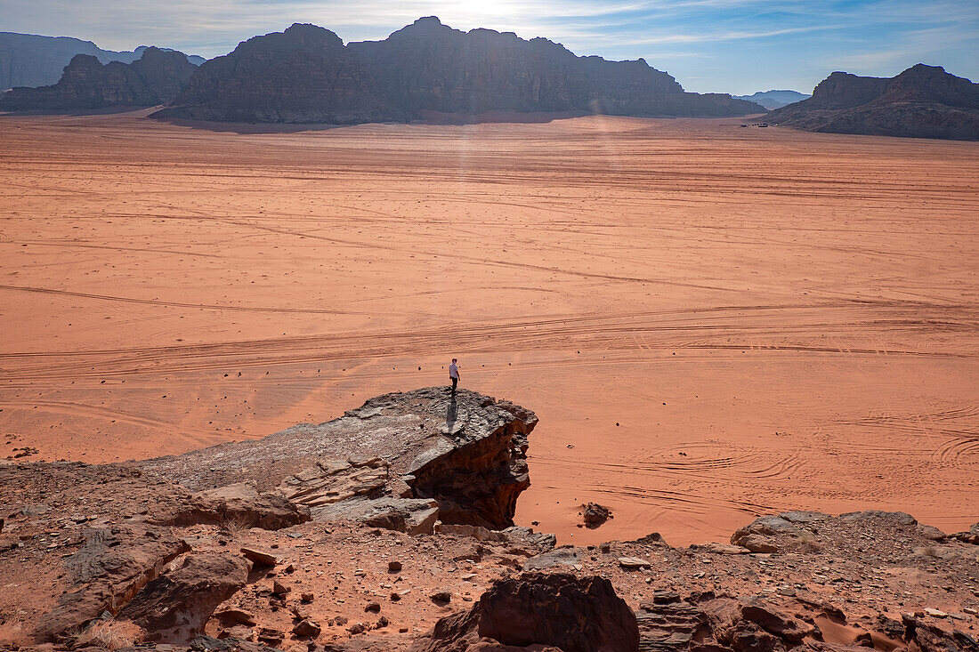 A person standing on a rock above the wide plain of Wadi Rum desert, UNESCO World Heritage Site, Jordan, Middle East