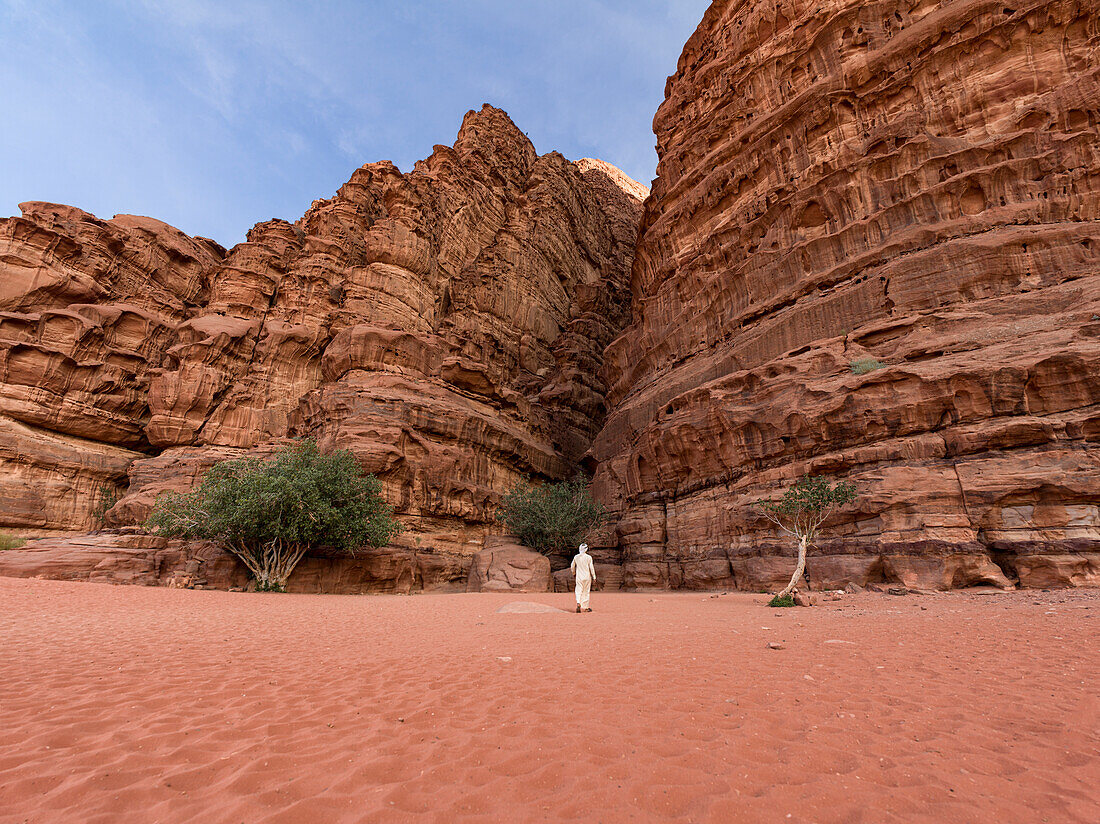 A beduin with traditional white clothes walking towards a canyon in Wadi Rum desert, UNESCO World Heritage Site, Jordan, Middle East