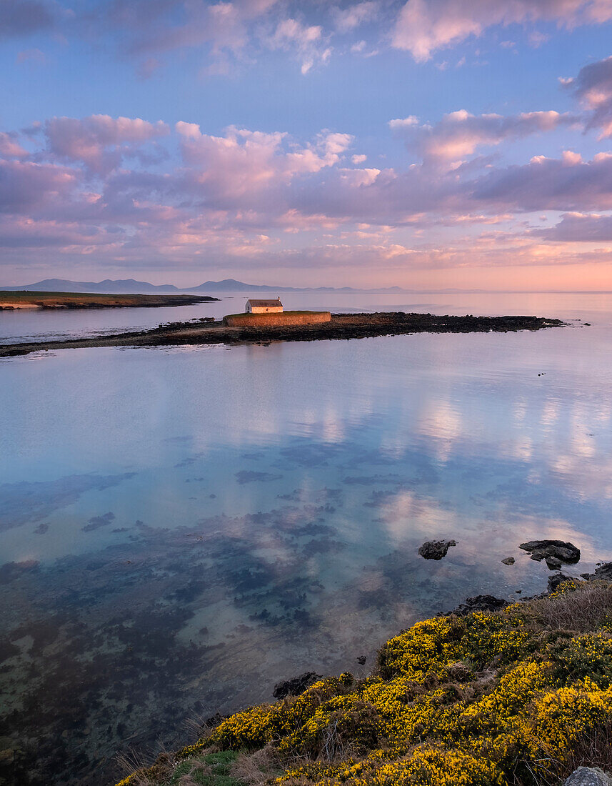 St. Cwyfans Church auf der Insel Cribinau mit der Halbinsel Lleyn im Hintergrund bei Sonnenuntergang, nahe Aberffraw, Anglesey, Nordwales, Vereinigtes Königreich, Europa