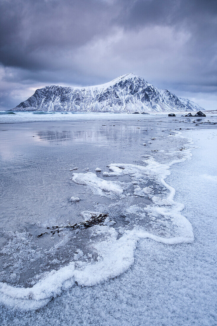 Gefrorene Wellenmuster am Strand von Skagsanden, im Hintergrund der Berg Hustinden im Winter, in der Nähe von Flakstad, Flakstadoya, Lofoten Inseln, Nordland, Norwegen, Skandinavien, Europa