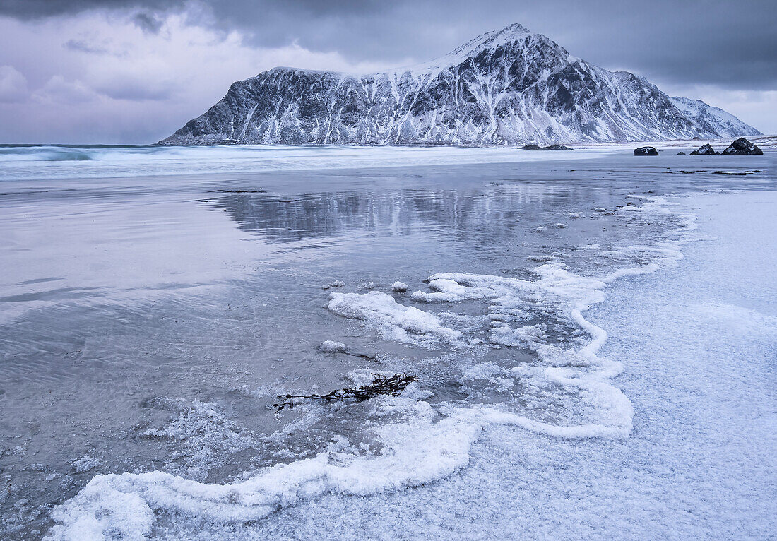 Frozen Wave Patterns on Skagsanden beach backed by Hustinden mountain winter, near Flakstad, Flakstadoya, Lofoten Islands, Nordland county, Norway, Scandanavia, Europe