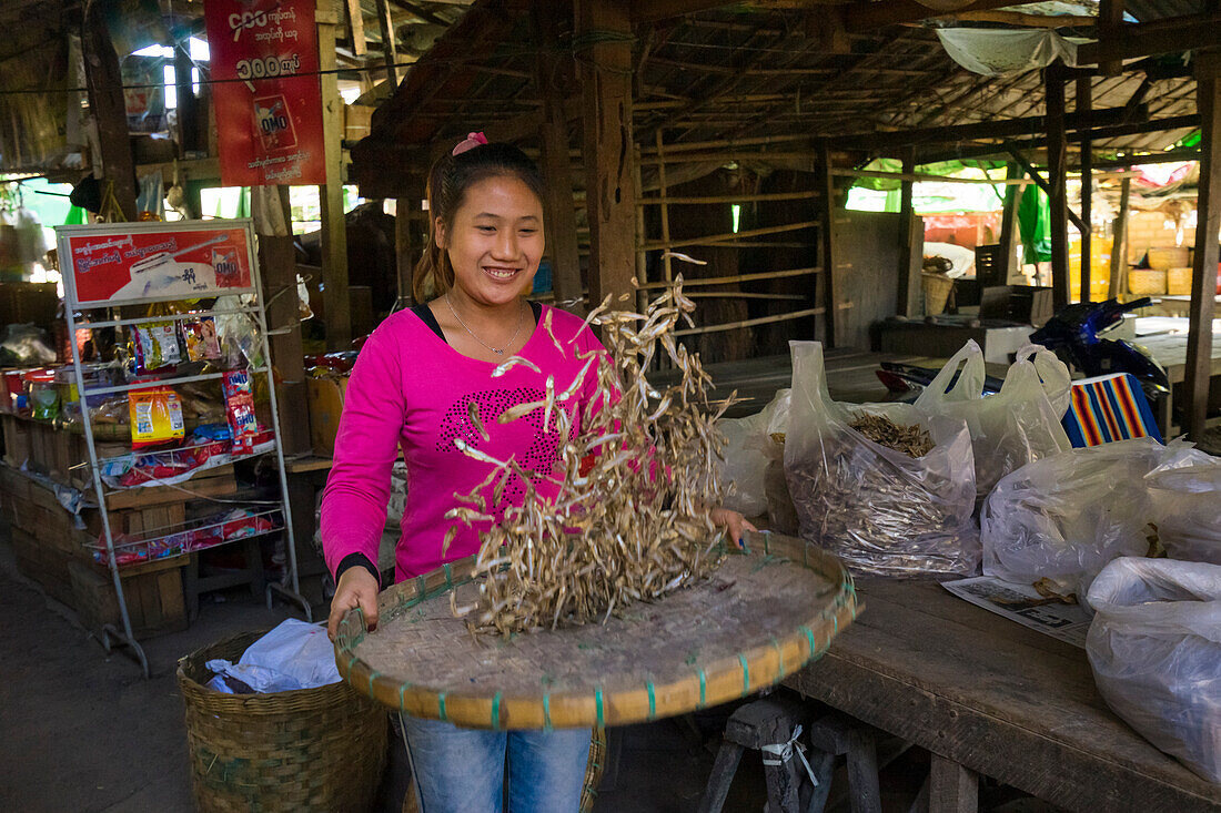 Young woman throwing dried fish in air at market, Hsipaw, Shan State, Myanmar (Burma), Asia