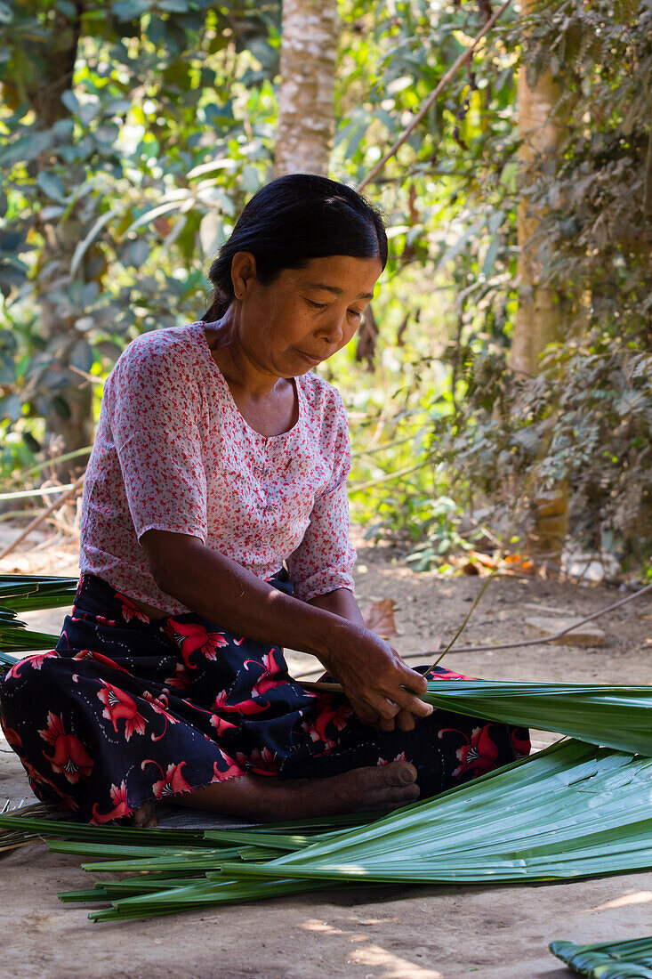 Birmesische Frau sitzt auf dem Boden und flechtet Palmblätter, um ein Dach zu decken, Chaung Tha, Myanmar (Birma), Asien