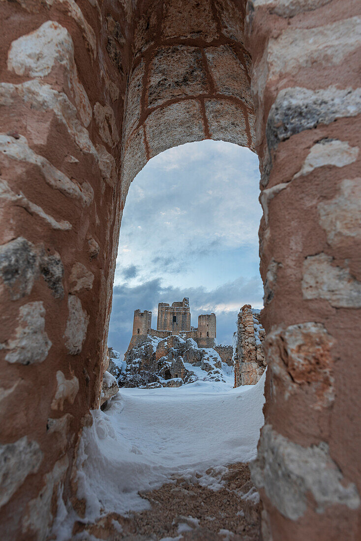 Die schneebedeckte Burg von Rocca Calascio zwischen den Ruinen des alten Dorfes von einem Bogen aus gesehen, Rocca Calascio, Nationalpark Gran Sasso e Monti della Laga, Campo Imperatore, Provinz L'Aquila, Abruzzen, Italien, Europa