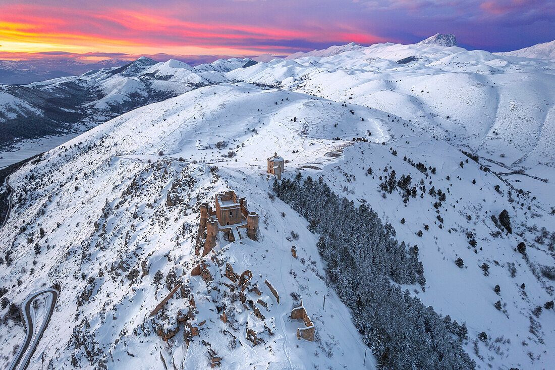 Aerial winter view of the snow covered Rocca Calascio castle and church of Santa Maria della Pieta,?with pink clouds at sunset, Rocca Calascio, Gran Sasso e Monti della Laga National Park, Campo Imperatore, L'Aquila province, Abruzzo, Italy, Europe