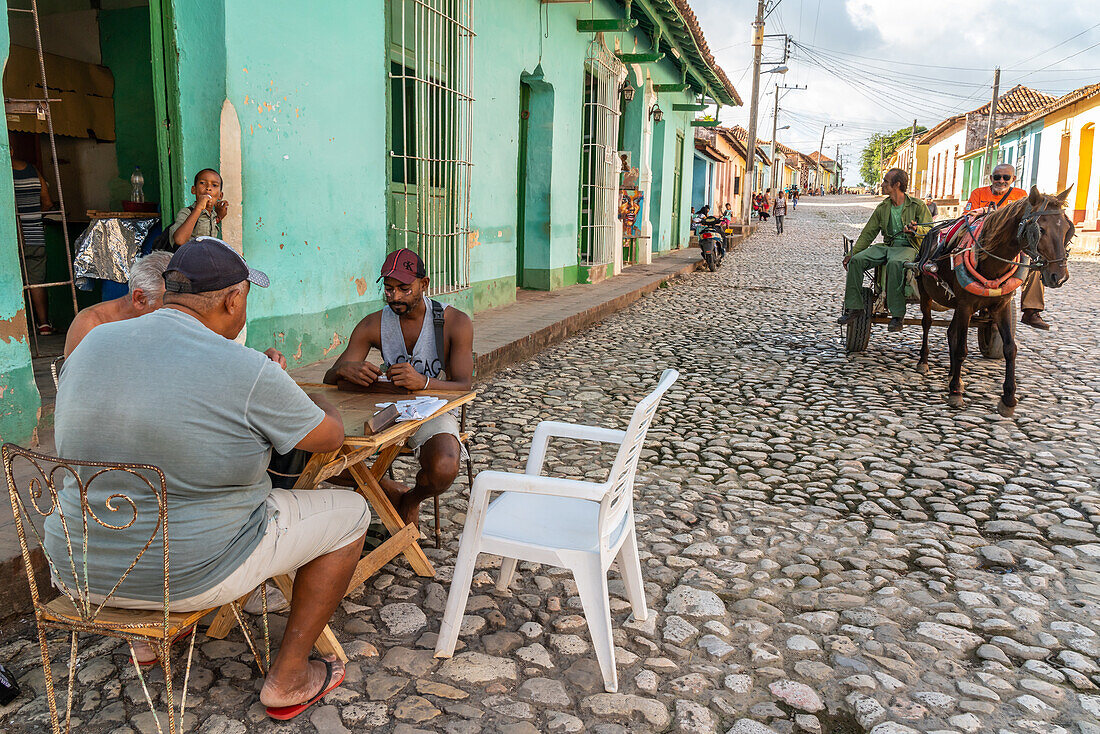 Dominospiel am Tante-Emma-Laden, während ein Pferdewagen auf dem Kopfsteinpflaster vorbeifährt, Trinidad, Kuba, Westindien, Karibik, Mittelamerika