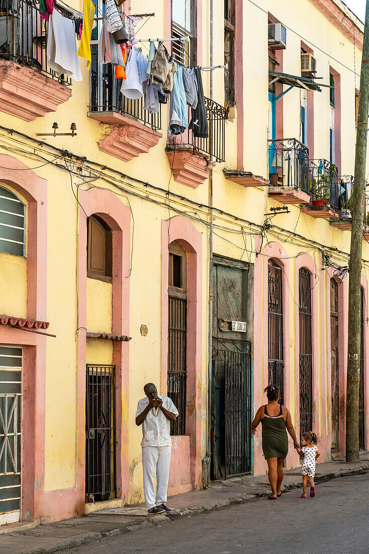 Mann zündet Zigarre in typischer Seitenstraße an, bunte Wäsche auf Balkonen drapiert, Alt-Havanna, Kuba, Westindien, Karibik, Mittelamerika