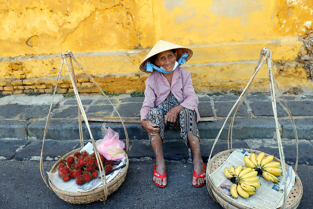 Typischer Straßenverkäufer mit vietnamesischem Hut sitzt und verkauft Lebensmittel, frisches Obst, Hoi An, Vietnam, Indochina, Südostasien, Asien