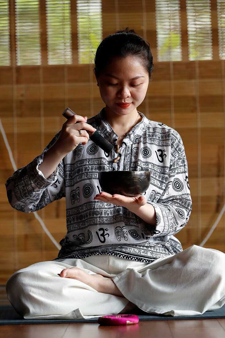 Tibetische Schale, buddhistische Frau beim Üben einer Klangschale für Klangtherapie in einer Atmosphäre für Heilung, Meditation, Yoga und Entspannung, Quang Ninh, Vietnam, Indochina, Südostasien, Asien