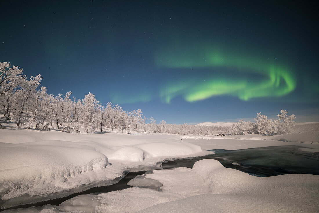 The northern lights appear above a river, Kiruna Municipality, Norrbotten County, Lapland, Sweden