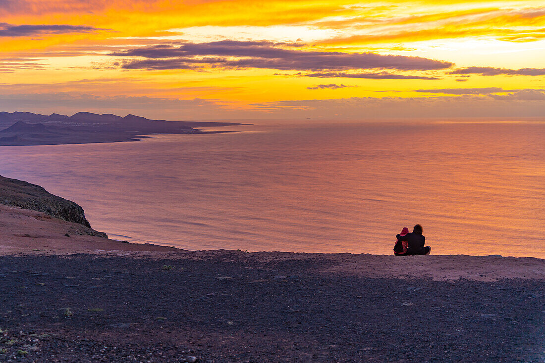 Blick auf ein Paar mit Blick auf die vulkanische Küste vom Mirador del Rio bei Sonnenuntergang, Lanzarote, Las Palmas, Kanarische Inseln, Spanien, Atlantik, Europa