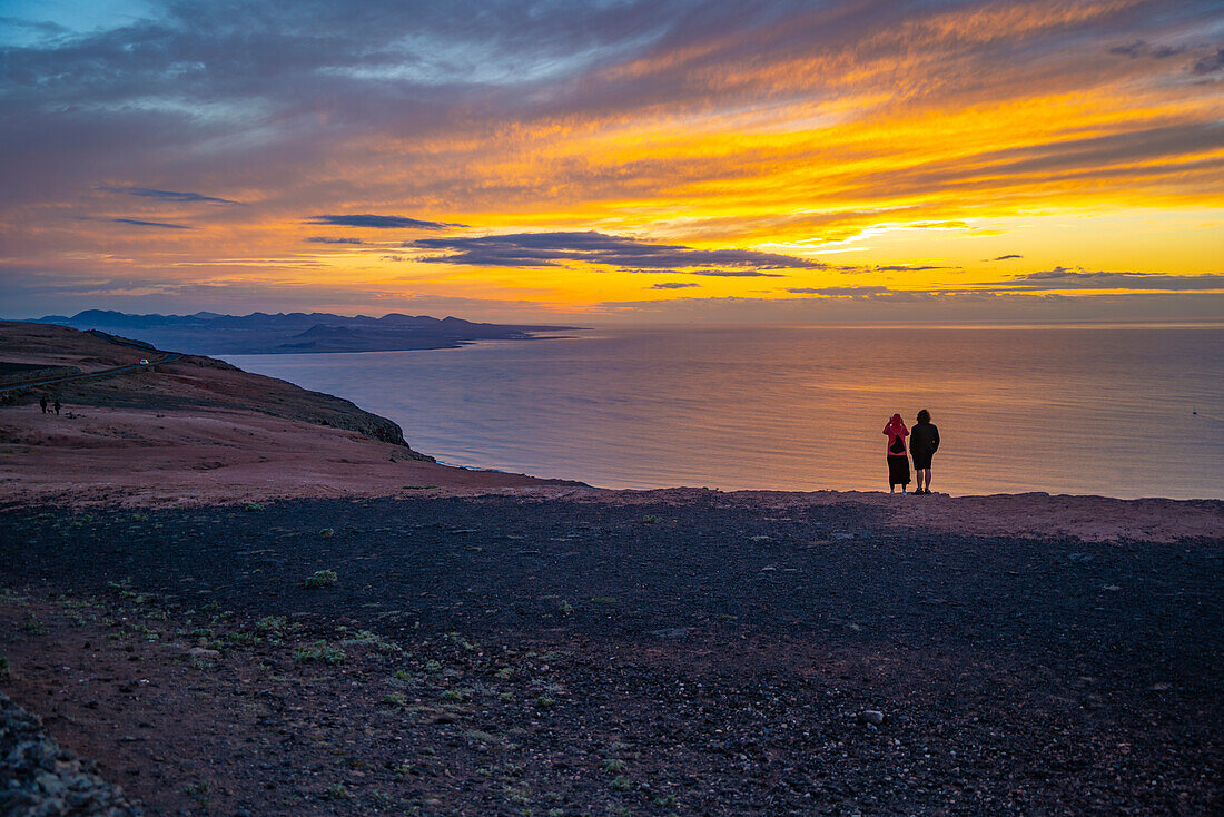 Blick auf ein Paar mit Blick auf die Vulkanküste vom Mirador del Rio bei Sonnenuntergang, Lanzarote, Las Palmas, Kanarische Inseln, Spanien, Atlantik, Europa