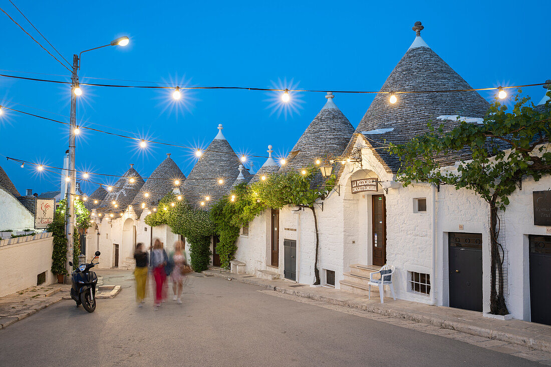 Whitewashed trulli houses along Via Monte San Michele street in the old town lit up at dusk, Alberobello, UNESCO World Heritage Site, Puglia, Italy, Europe