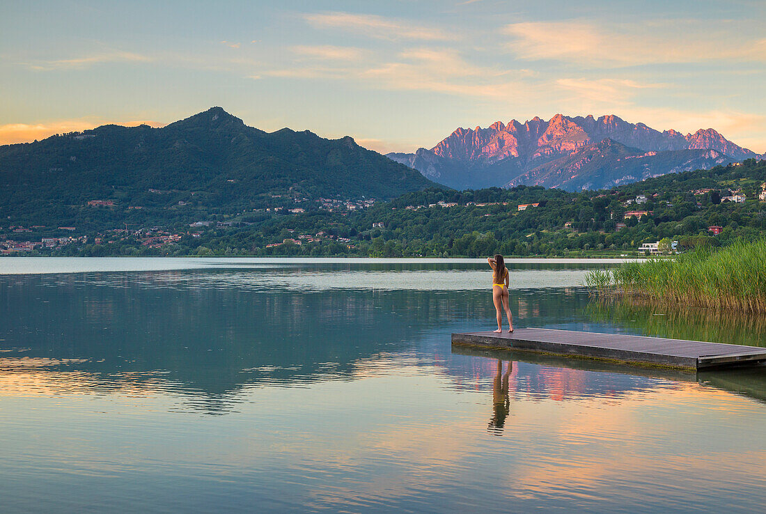 Mädchen entspannt sich und betrachtet den Sonnenuntergang auf den Lecco Bergen (Resegone und Barro Berg), die sich im Oggiono See im Sommer spiegeln, Annone See, Oggiono, Brianza, Lecco Provinz, Lombardei, Italien, Europa (MR)