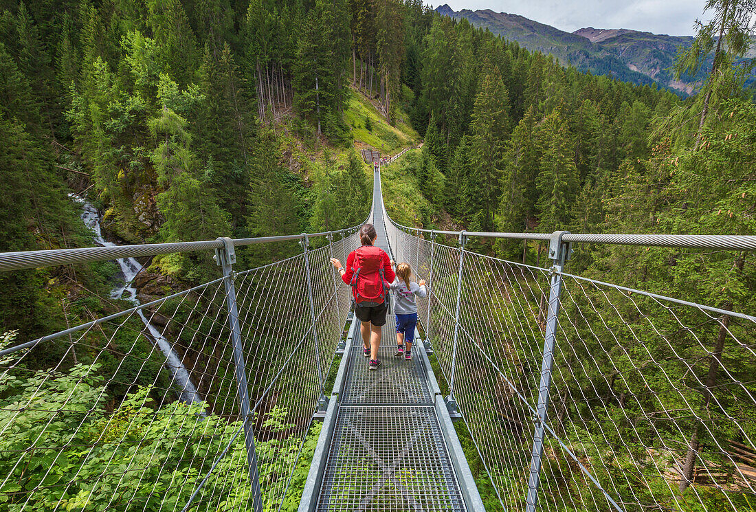 Mom and daughter cross the tibetan bridge (Ponte Sospeso Ragaiolo), Rabbi valley (val di Rabbi), Trento province, Trentino-Alto Adige, Italy, Europe (MR)