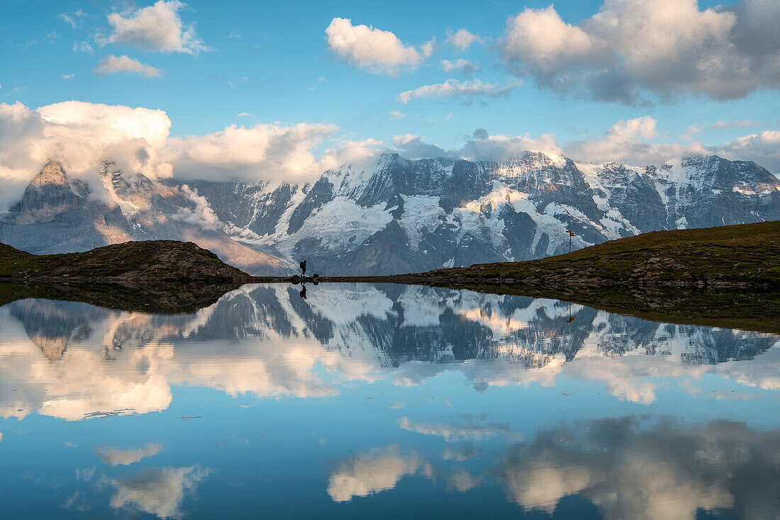 Mann spaziert, während sich die Jungfraugruppe im Grauseeli-See spiegelt, Murren, Lauterbrunnen, Schweiz, Europa