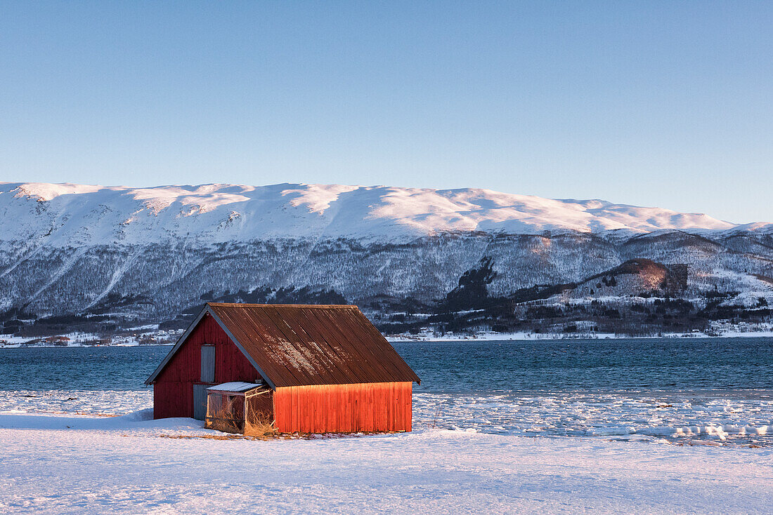 Typische Fischerhäuser vor einem Fjord in der Nähe von Tromso, Provinz Troms, Norwegen, Europa