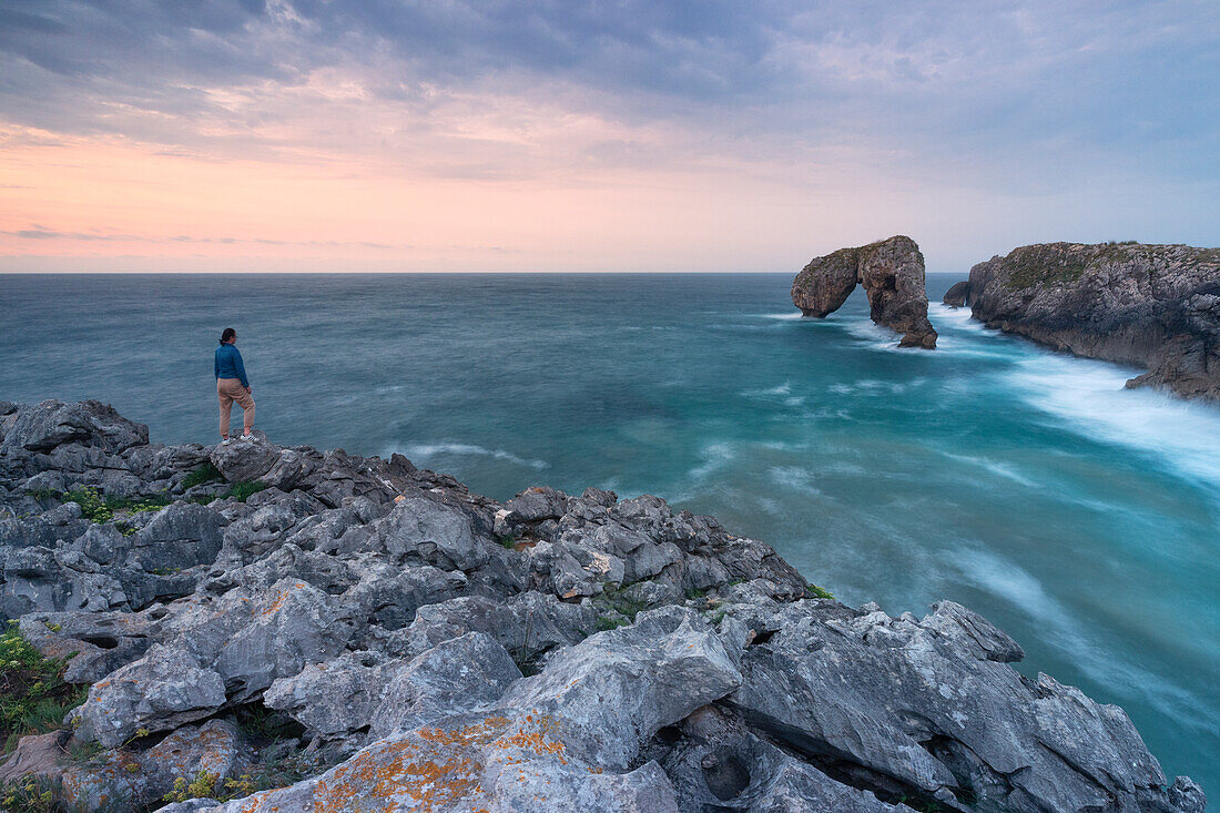 ein Tourist bewundert den Sonnenuntergang bei El Castro de las Gaviotas, Gemeinde Naves, Principado de Asturias, Spanien, Europa