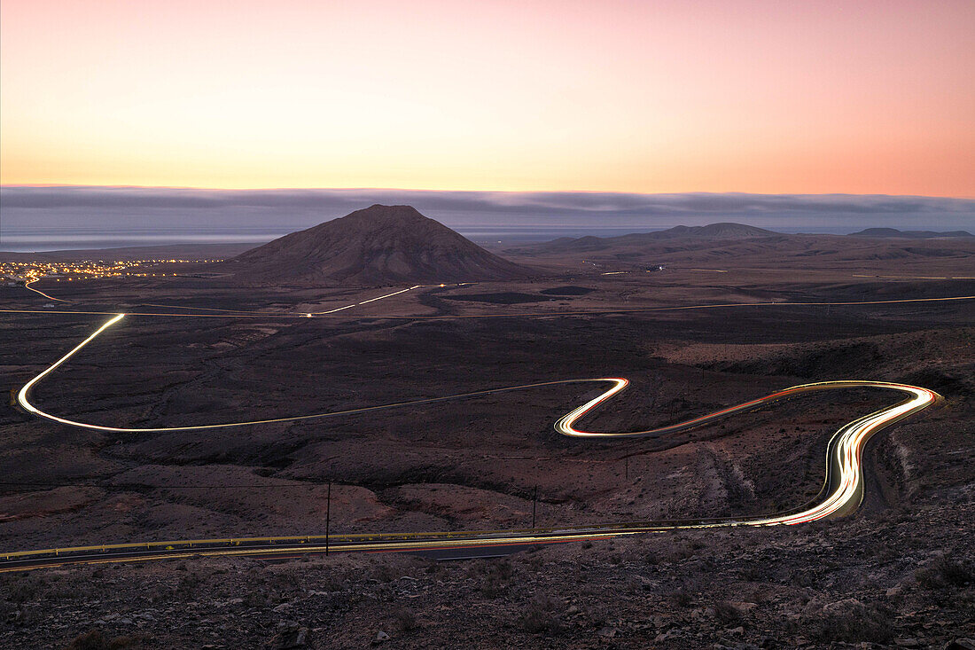 eine Langzeitbelichtung, um die Autospuren während eines sommerlichen Sonnenuntergangs entlang der Straße in der Nähe des Tindaya-Berges einzufangen, Fuerteventura, Kanarische Insel, Spanien, Europa