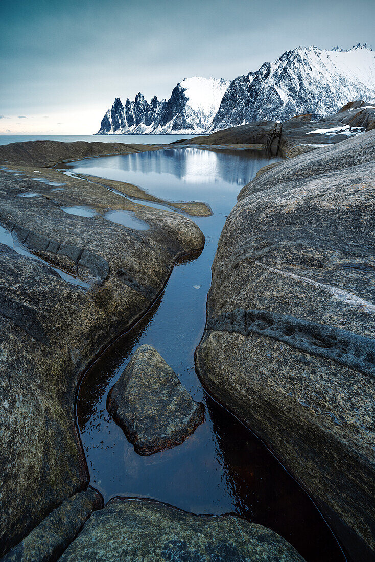 ein großes Wasserbecken spiegelt den Berg der Teufelszähne an einem Wintertag, Senja, Norwegen, Europa