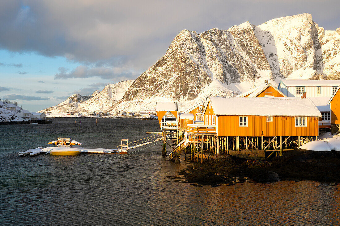 das erste Licht umhüllt das Dorf Sakrisoy mit dem schneebedeckten Berggipfel, Lofoten, Norwegen, Europa