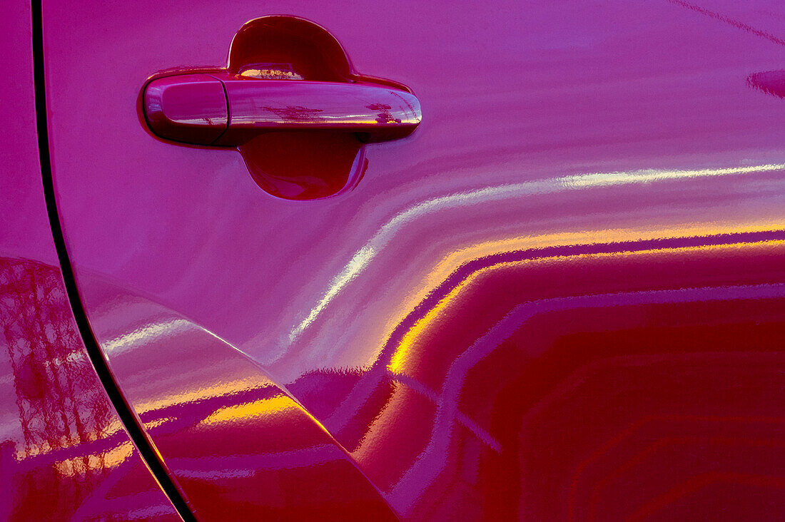 Abstraktes Muster eines Sonnenuntergangs, der sich in einem roten Auto spiegelt.