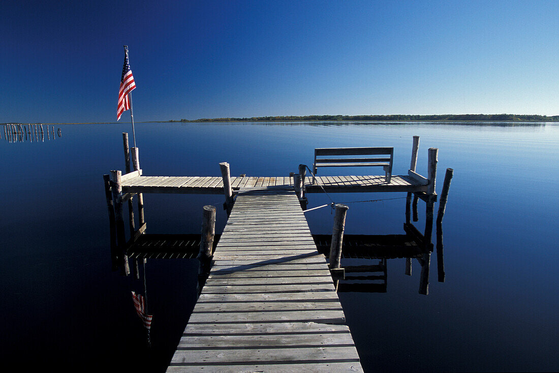 Early morning boat dock and star-spangled banner flag over calm reflection water on Lake of the Woods near Warroad Minnesota USA