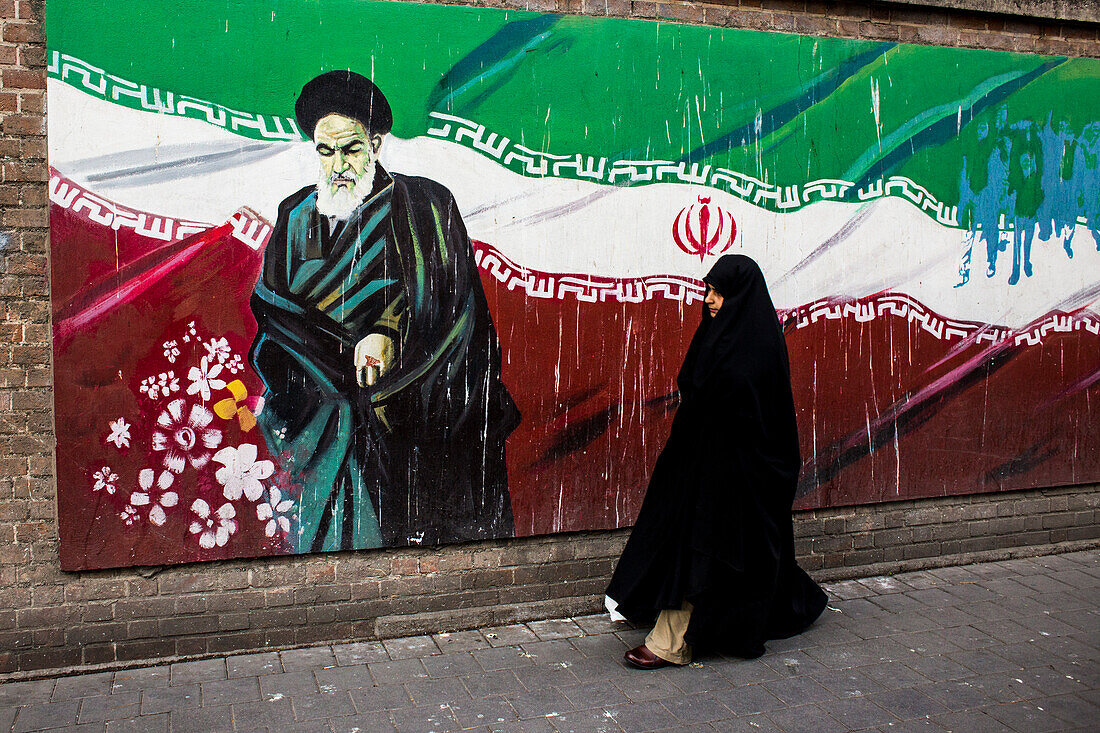 Frau spaziert vor dem Wandgemälde von Ayatollah Khomeini an der Wand der ehemaligen US-Botschaft in Teheran