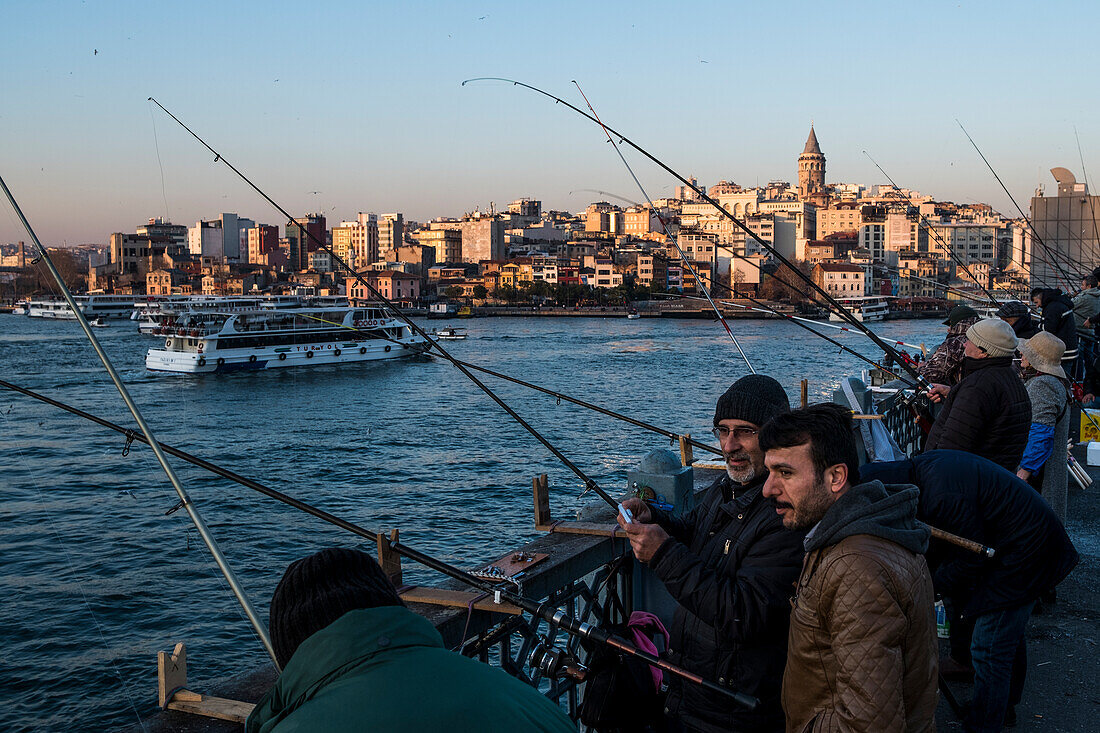 Menschen fischen von der Galata-Brücke aus vor dem Galata-Viertel und dem Galata-Turm während des Sonnenuntergangs am Goldenen Horn