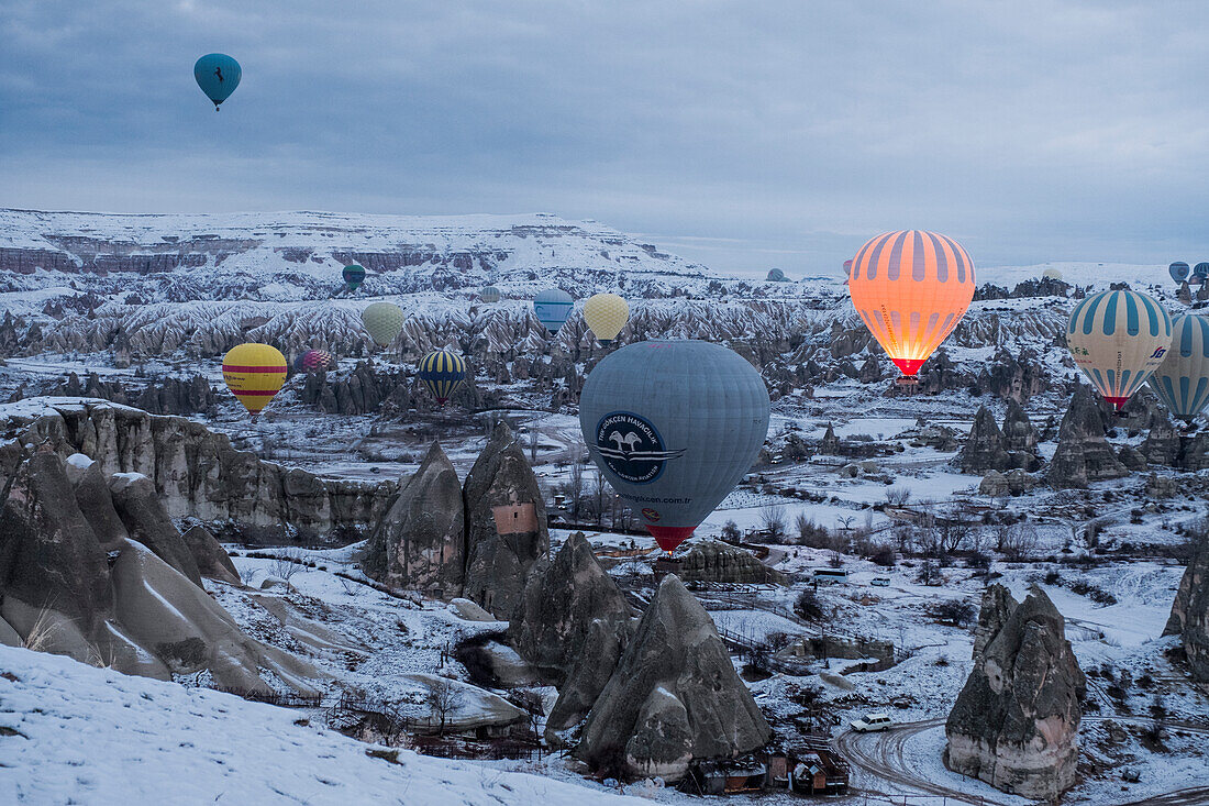 Kappadokien im Winter mit Schnee bedeckt und einem Heißluftballon, der in der Nähe von Göreme abhebt