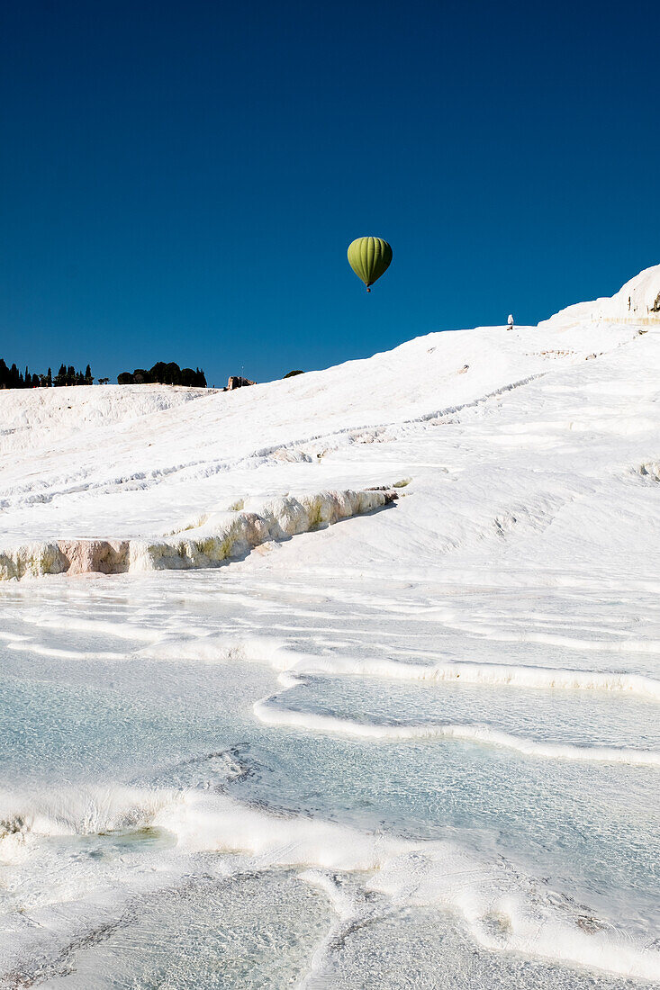 Travertine terrace formations at Pamukkale, tourists and hot-air balloon