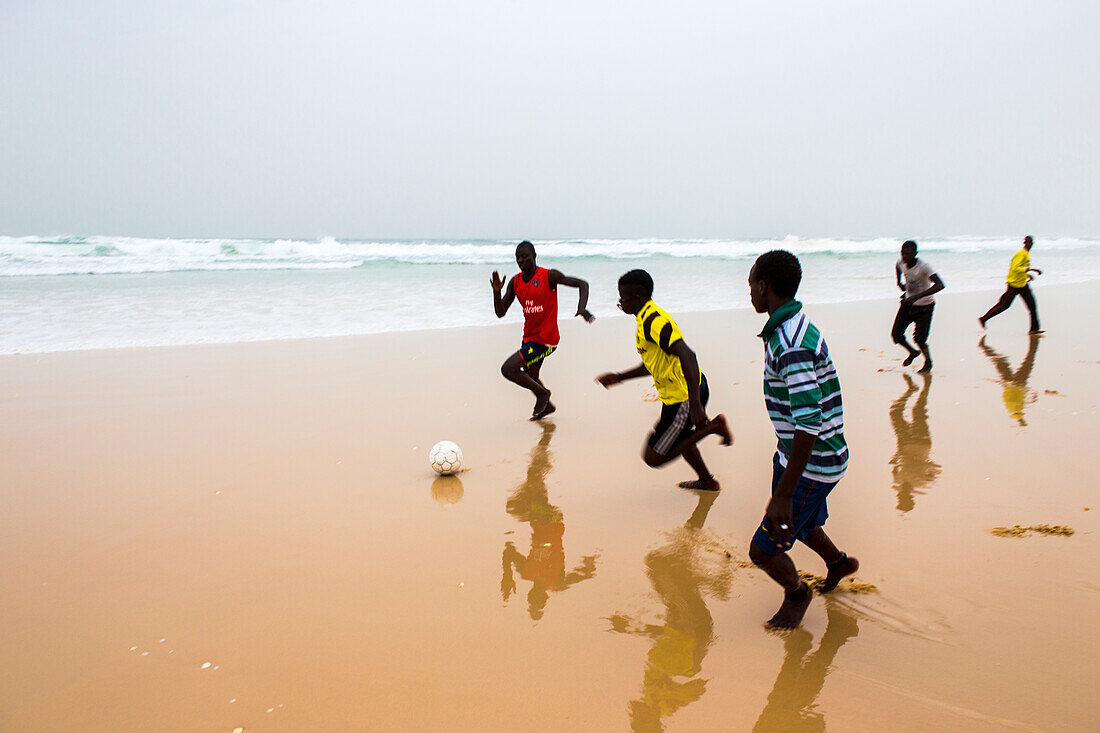 Boys playing football on the beach during the afternoon fish market in Mboro Plage beach when the canoes arrive loaded