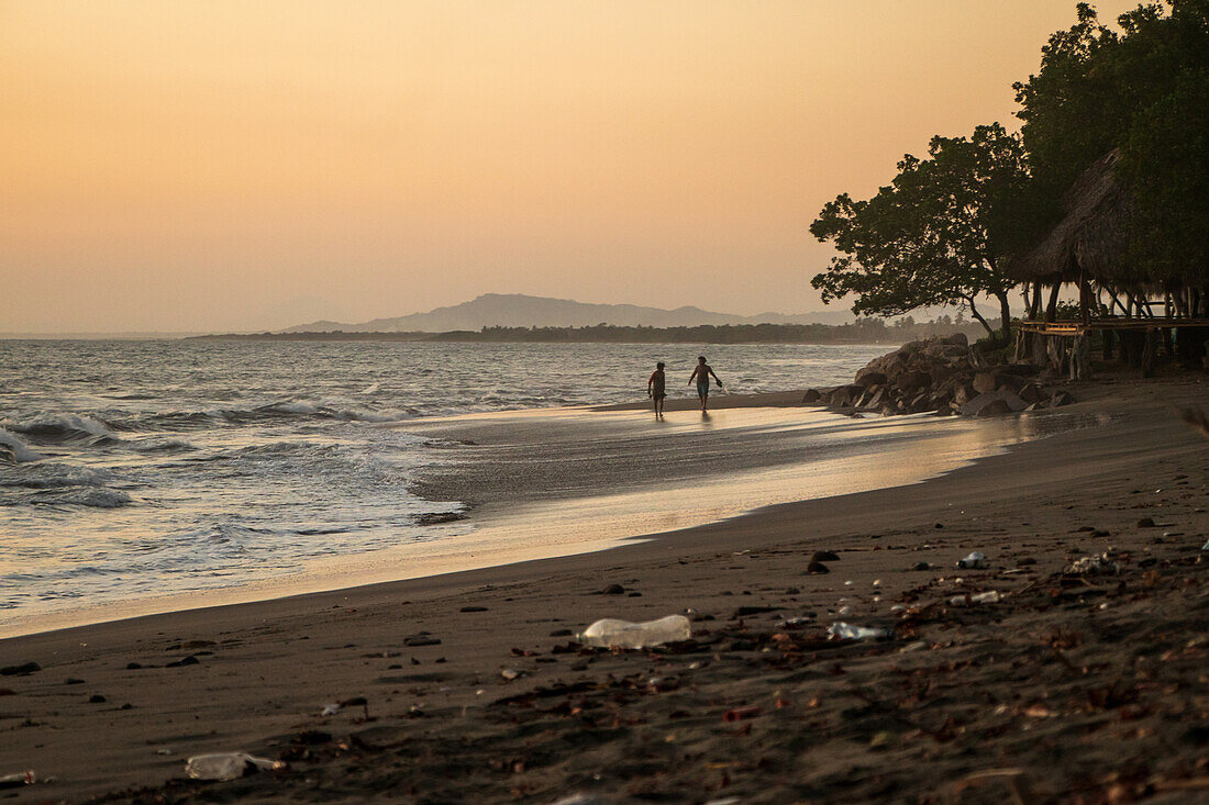 Paar beim Spaziergang bei Sonnenuntergang an einem mit Plastik bedeckten Strand in Nicaragua