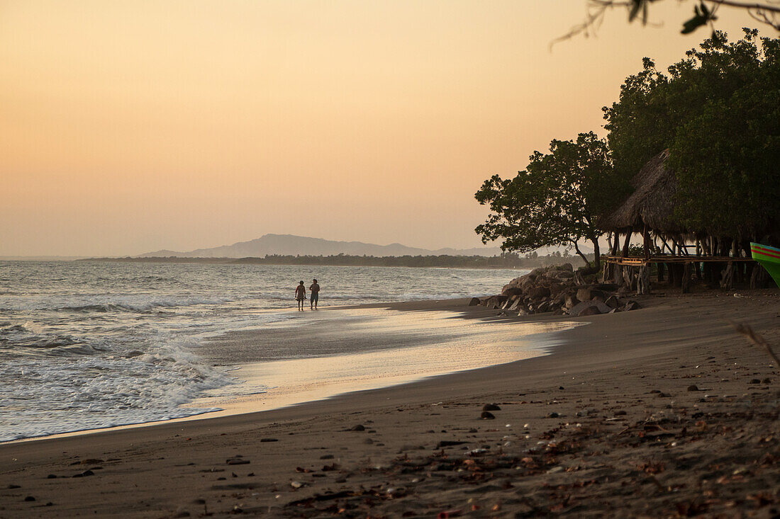 Paar beim Spaziergang bei Sonnenuntergang am Strand von Jiquilillo, Chinandega, Nicaragua